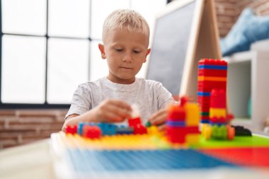 Sınıftaki masada oturan, inşaat bloklarıyla oynayan sevimli çocuk.