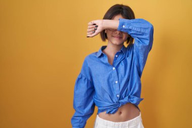 Sarı arka planda duran genç kız kollarıyla gözlerini kapatıyor neşeli ve komik gülümsüyor. kör kavram. 