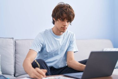 Evde dizüstü bilgisayar kullanan genç sarışın adam.