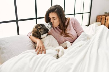 Genç bir kadın yatak odasında öpüşüyor ve köpeğe sarılıyor.