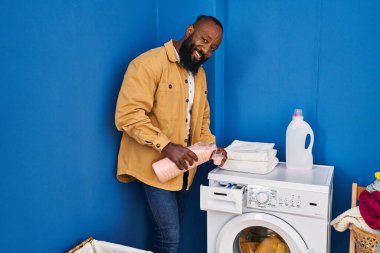 Genç Afrikalı Amerikalı adam gülümsüyor Çamaşır odasında çamaşır makinesine deterjan döküyor