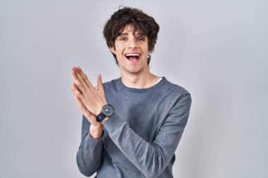 Young man standing over isolated background clapping and applauding happy and joyful, smiling proud hands together 