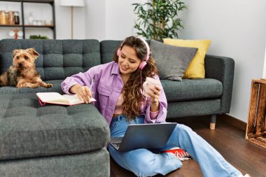 Genç ve güzel İspanyol kadın dizüstü bilgisayar kullanıyor. Evde köpekle yerde oturuyor.