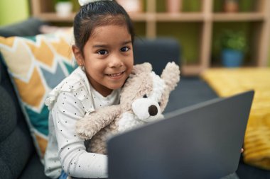 Adorable hispanic girl using laptop sitting on sofa at home