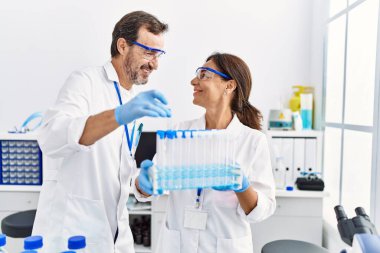 Laboratuvarda deney tüpü tutan bilim adamı üniforması giyen orta yaşlı erkek ve kadın partnerler.