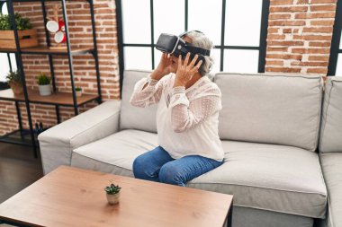 Evde sanal gerçeklik gözlüğü kullanan orta yaşlı bir kadın video oyunu oynuyor.