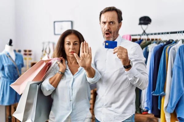 持购物袋和信用卡的西班牙裔中年夫妇手牵手 怒气冲冲地 沮丧地做着停下来的手势 — 图库照片