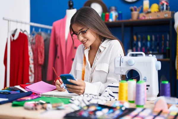 Young Beautiful Hispanic Woman Tailor Using Smartphone Drawing Notebook Clothing — Stockfoto