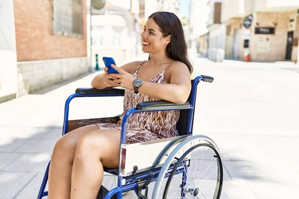 若い美しいヒスパニック系の女性が路上で車椅子に座っているスマートフォンを使って — ストック写真