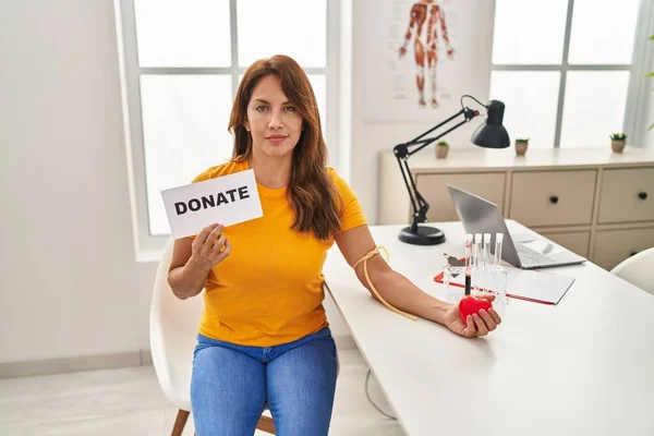 Hispanic woman supporting blood donation relaxed with serious expression on face. simple and natural looking at the camera.