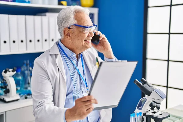 Senior man scientist talking on the smartphone writing on document at laboratory