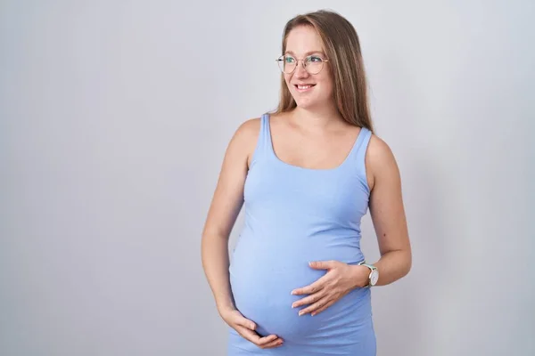 Mladá Těhotná Žena Stojící Nad Bílým Pozadím Dívající Stranou Úsměvem — Stock fotografie