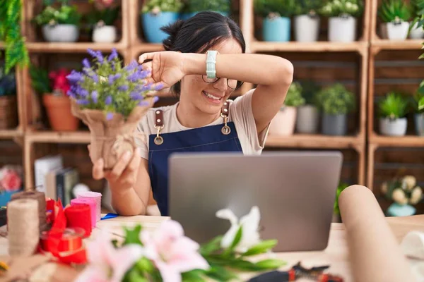 Young hispanic woman working at florist shop doing video call smiling cheerful playing peek a boo with hands showing face. surprised and exited