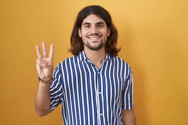 Латиноамериканец Длинными Волосами Стоит Желтом Фоне Показывает Пальцами Номер Три — стоковое фото