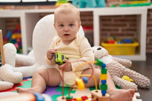 幼稚園の床に座っている車のおもちゃで遊ぶ愛らしい白人の赤ん坊 — ストック写真