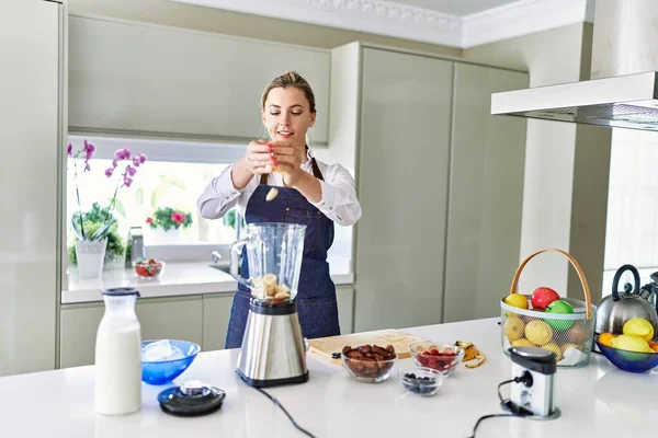 Genç Sarışın Kadın Mutfaktaki Blendere Muz Dökerek Gülümsüyor — Stok fotoğraf