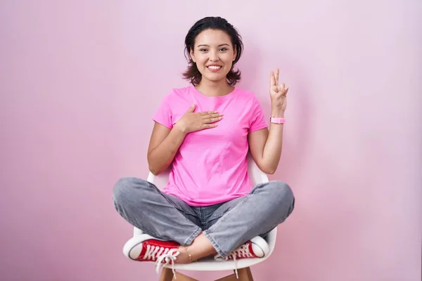 Hispanic Young Woman Sitting Chair Pink Background Smiling Swearing Hand — 图库照片