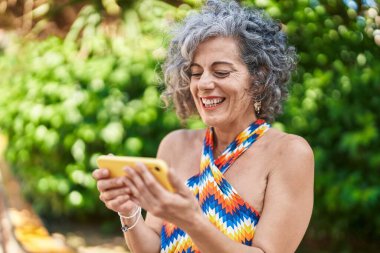 Middle age grey-haired woman smiling confident watching video on smartphone at park