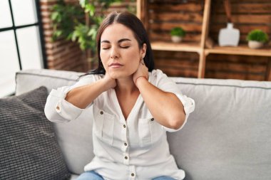 Evdeki kanepede oturan genç ve güzel İspanyol kadın boyun ağrısı çekiyor.