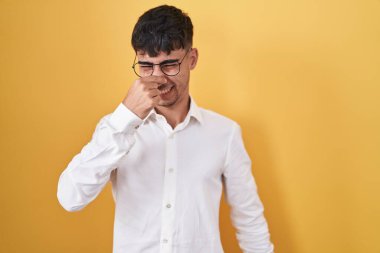 Sarı arka planda dikilen İspanyol genç adam pis ve iğrenç bir koku alıyor. Nefesini burnunda tutuyor. Kötü kokuyor. 