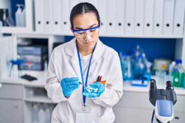 Laboratuvarda elinde cımbızla ilaç tutan genç İspanyol bilim kadını.