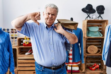 Gri saçlı, elinde alışveriş torbaları olan yaşlı bir adam kızgın suratlı, olumsuz işaretli, baş parmakları aşağıda, reddedilme konsepti var. 