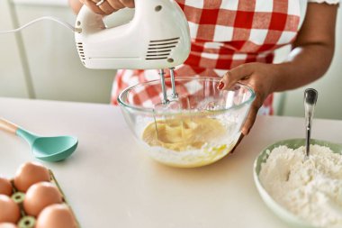 Hispanic brunette woman preparing cake with electric whisk at the kitchen
