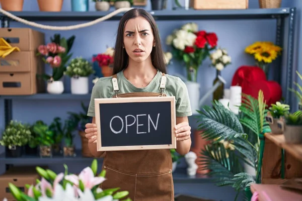 花屋で働いている若いブルネットの女性は 問題のために動揺を眉をひそめて 懐疑的で緊張したオープンサインを保持しています 否定的な人 — ストック写真