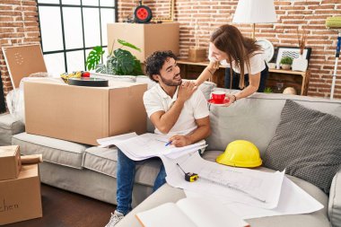 Man and woman couple drinking coffee looking house plans at new home