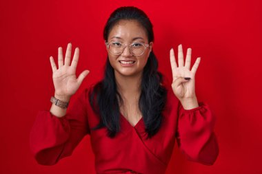 Asian young woman standing over red background showing and pointing up with fingers number nine while smiling confident and happy. 