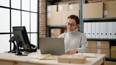 Orta yaşlı İspanyol kadın ecommerce iş işçisi Depo ofisinde dizüstü bilgisayar kullanıyor