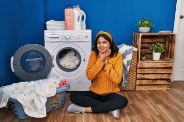 Young hispanic woman doing laundry shouting suffocate because painful strangle. health problem. asphyxiate and suicide concept. 