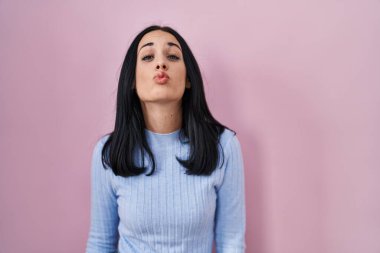 Hispanic woman standing over pink background looking at the camera blowing a kiss on air being lovely and sexy. love expression. 