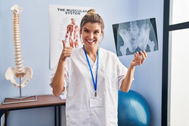 Young woman holding pelvis radiography smiling happy and positive, thumb up doing excellent and approval sign 