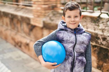 Sarışın çocuk gülümsüyor kendine güvenen topu sokakta tutuyor