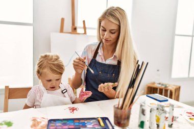 Mother and daughter smiling confident painting palm hands at art studio