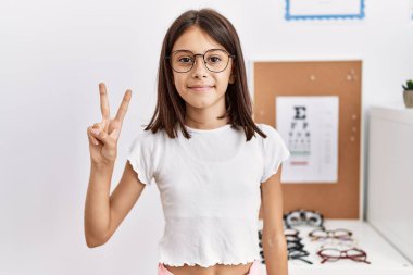 Genç İspanyol kız gözlük takıyor ve iki numarayı göstererek gülümsüyor. Kendinden emin ve mutlu.. 