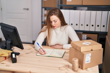 Genç sarışın kadın ecommerce iş işçisi ofiste kitap yazıyor.