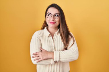 Sarı arka planda duran genç İspanyol kadın gülümsüyor, yan tarafa bakıyor ve düşünüyor.. 