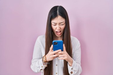 Çinli genç bir kadın akıllı telefon kullanarak kızgın ve kızgın bir şekilde bağırıyor öfkeyle bağırıyor. öfke ve agresif konsept. 