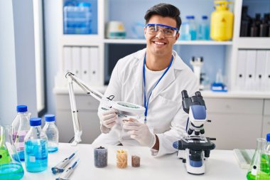 Young hispanic man scientist looking sample with loupe at laboratory