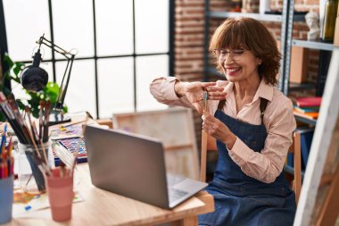 Orta yaşlı kadın sanatçı, resim stüdyosunda video araması yaptığından emin bir şekilde gülümsüyor.