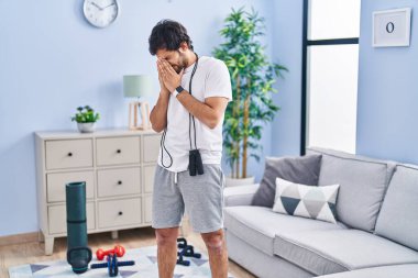 Handsome latin man wearing sportswear at home tired rubbing nose and eyes feeling fatigue and headache. stress and frustration concept. 