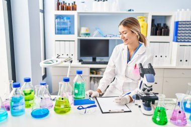 Genç İspanyol kadın bilim adamı. Sıvıyı ölçüyor. Laboratuvarda belgeye yazıyor.