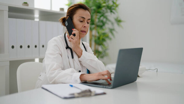 Латиноамериканка средних лет в форме врача разговаривает по смартфону в клинике