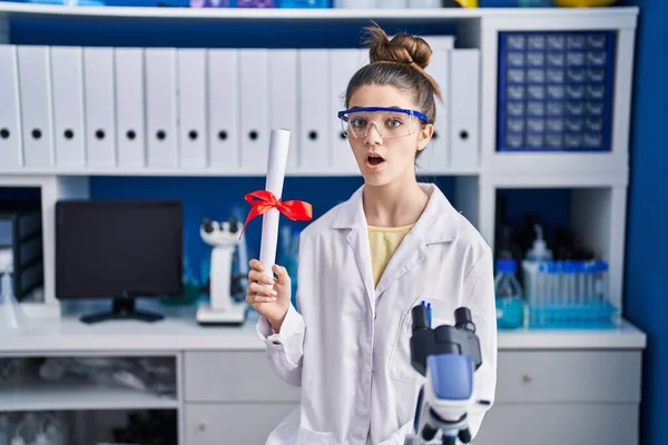 Teenager Girl Working Scientist Laboratory Holding Degree Scared Amazed Open —  Fotos de Stock