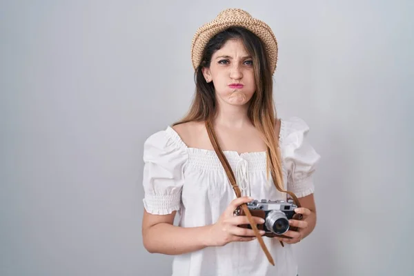 Young brunette woman holding vintage camera puffing cheeks with funny face. mouth inflated with air, catching air.