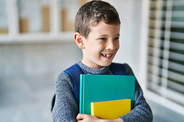 Blond child student holding books standing at school