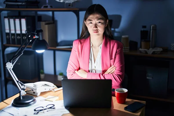 Chinese young woman working at the office at night skeptic and nervous, disapproving expression on face with crossed arms. negative person.