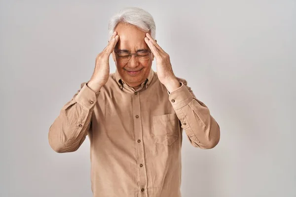 Hispanic senior man wearing glasses suffering from headache desperate and stressed because pain and migraine. hands on head.